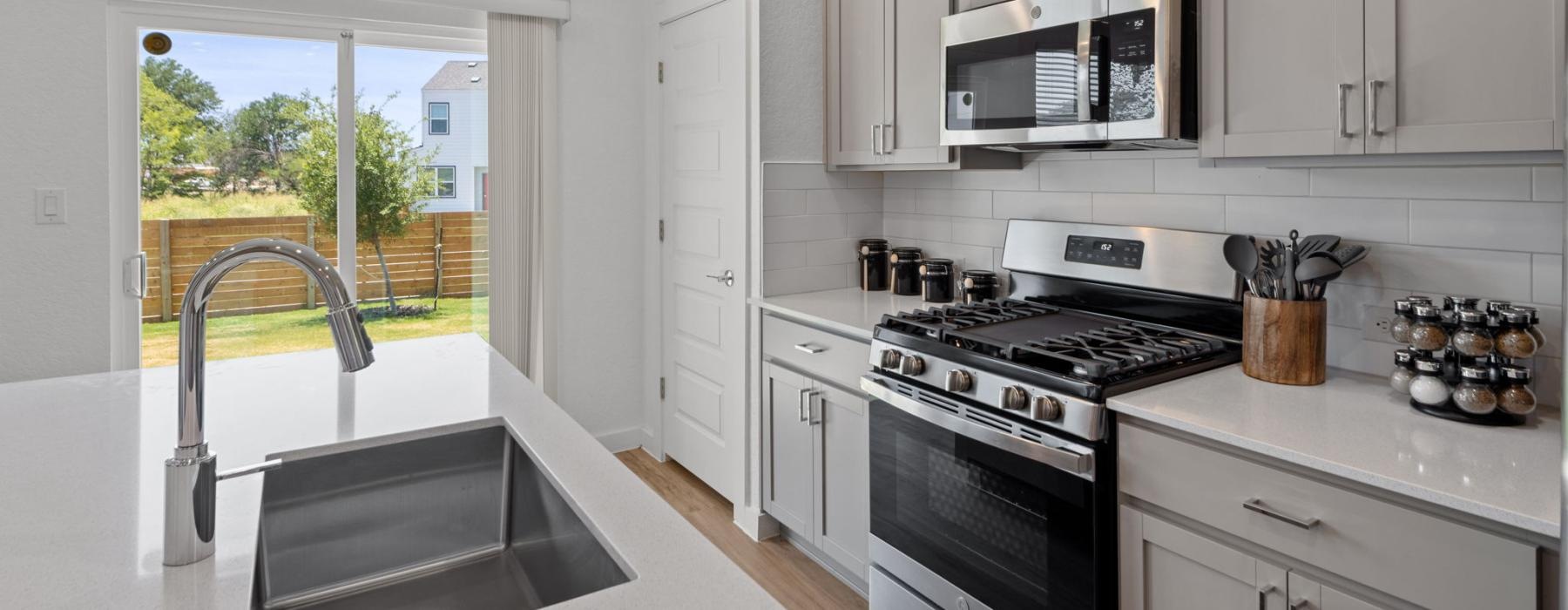 a kitchen with white cabinets a sink a stovetop and large windows