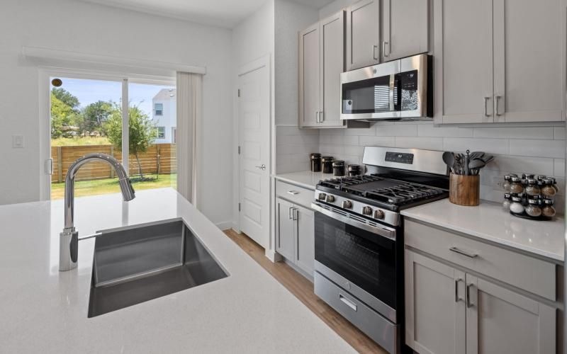 a kitchen with white cabinets a sink a stovetop and large windows